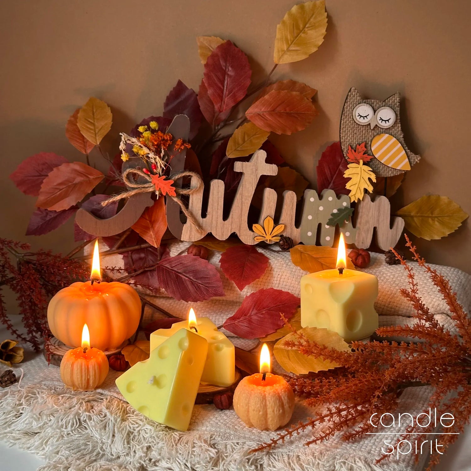 Burning fall scented yellow cheese and orange pumpkin candles on a colourful background with autumn decorations