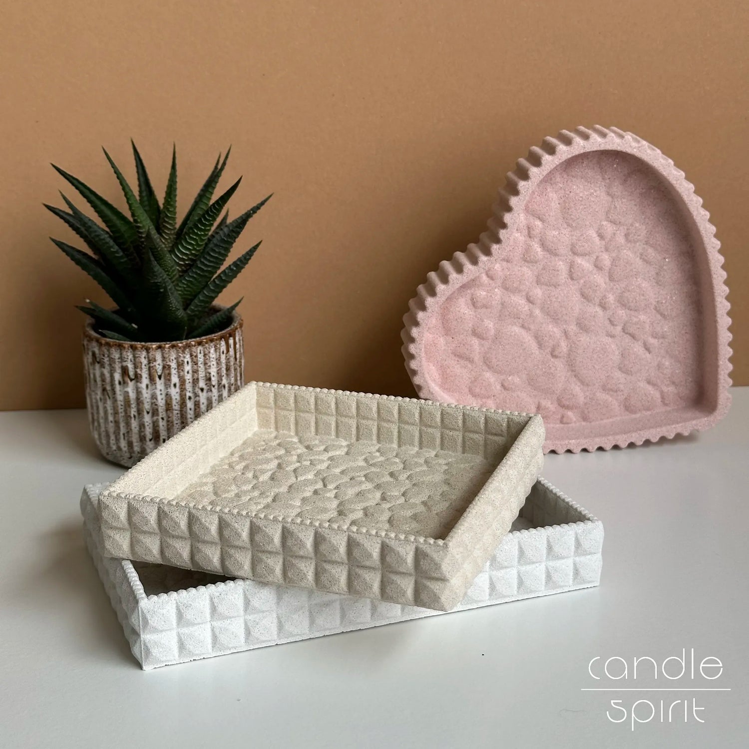 White textured rectangular trinket tray, beige square decorative tray, and pink heart-shaped tray on a office desk - storage and space organization.
