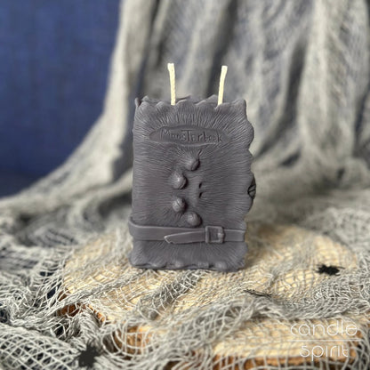 Scented gray monster book candle on a textured surface with a blue background - Halloween candle and unique gift for fantasy lovers