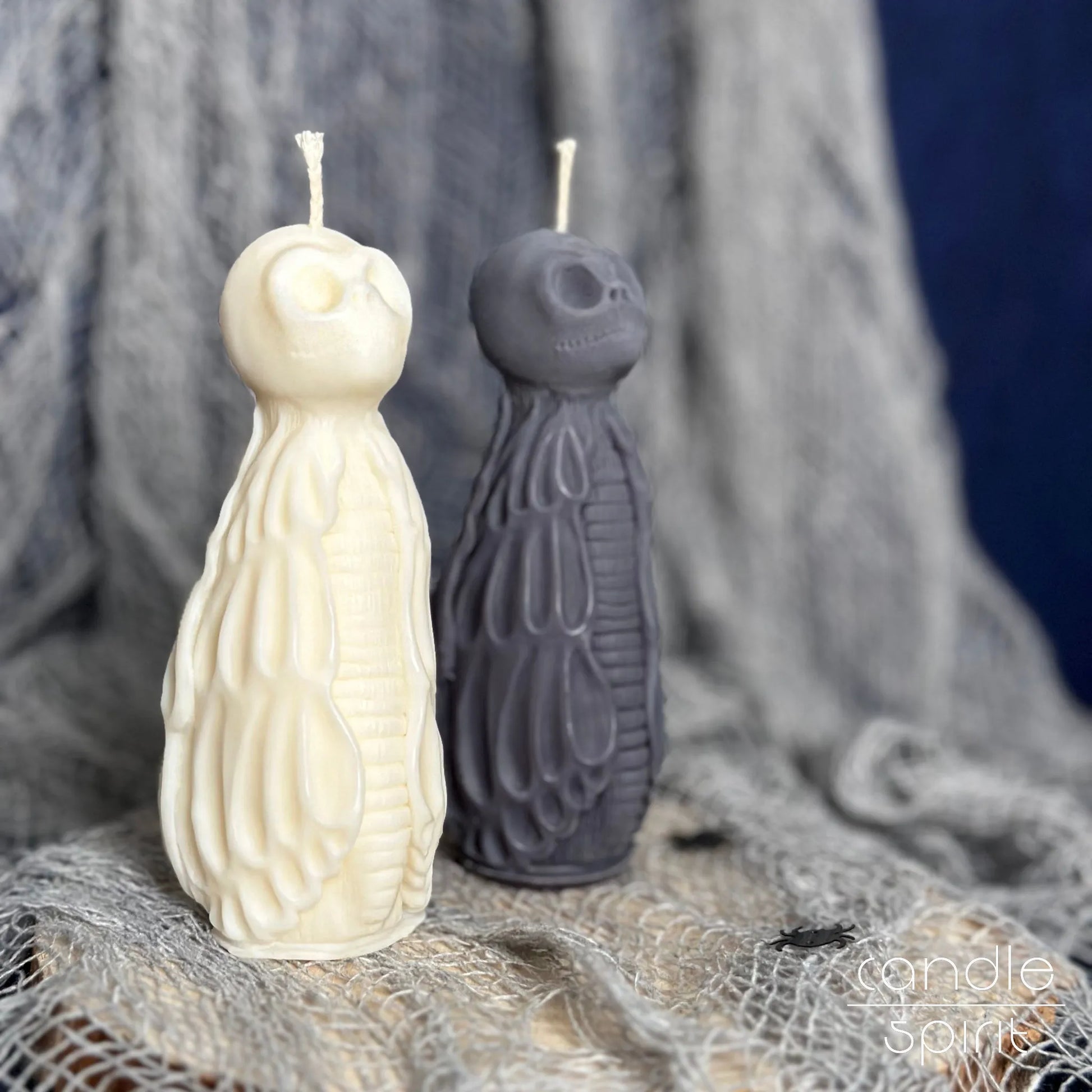 Two scented Halloween skull candles, one white and one gray, on a textured fabric background - unique gift for gothic lovers, rockers, and bikers.