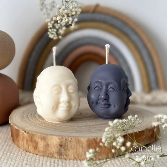 Two Hotei Laughing Buddha candles, one white and one gray with a rainbow arch in the background - feng shui gift for yoga lovers, spiritual seekers, and newlyweds.